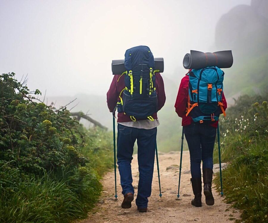 Dois caminhantes com mochilas e roupas em camadas avançam na neblina