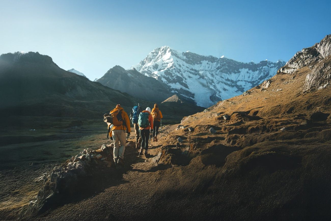 Caminhantes com mochilas avançam em direção a uma montanha nevada dos Andes